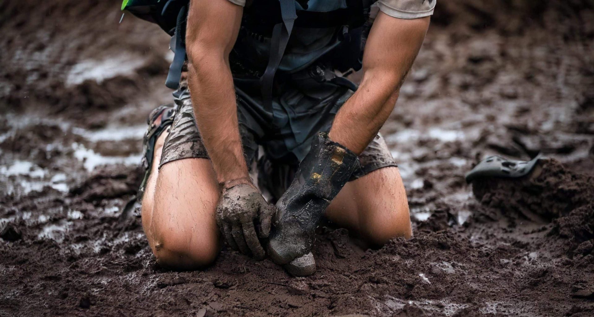 Firefly A close-up shot of a muddy, sweat-streaked knee pressing into wet, rugged ground as the athl